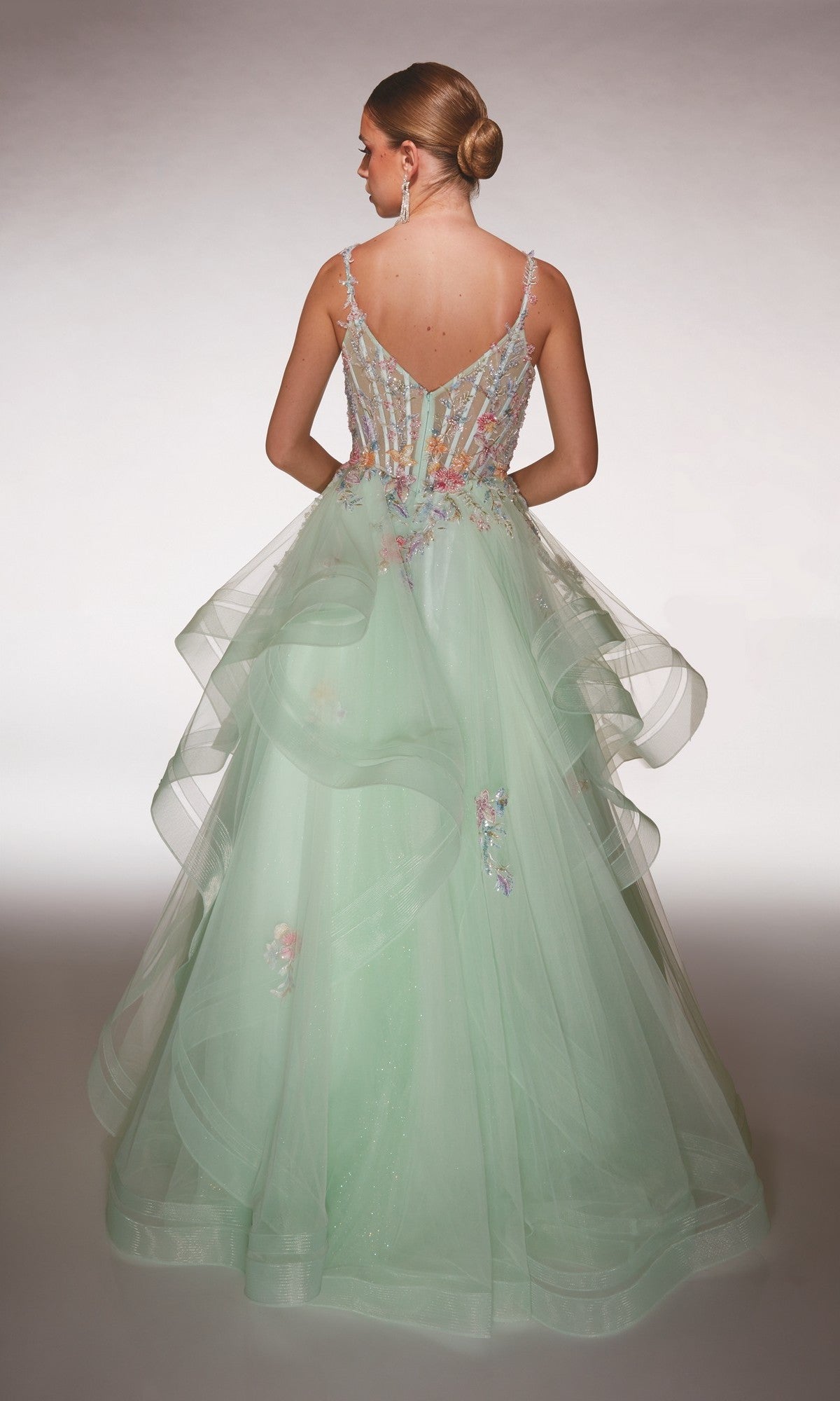 Woman with her back to the camera wears the Alyce 62201 Long Formal Dress in light green, featuring a layered tulle skirt and 3D floral appliques. Her hair is styled in a low bun.